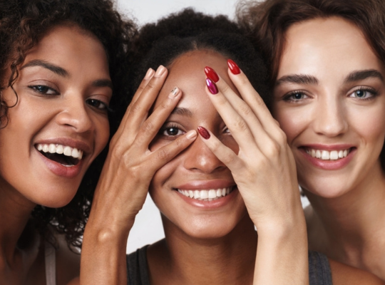 Three women smiling with different skin tones are awaiting best skin care and hair care treatments.